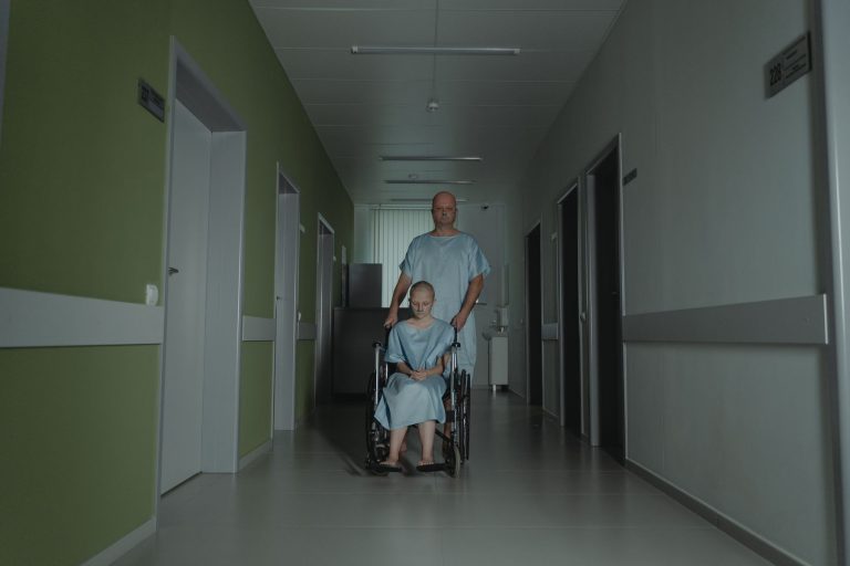 Patient wird im Rollstuhl durch einen Klinikflur begleitet